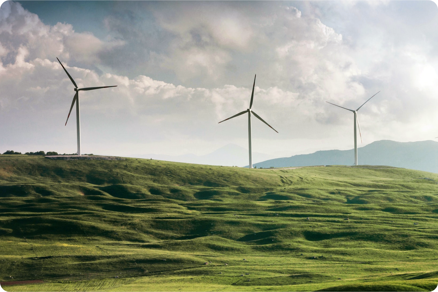 Three large wind turbines standing tall on top of a grassy hill.